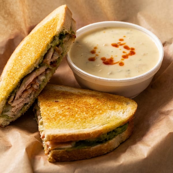 Grilled sandwich halves with avocado and meat, next to a cup of creamy soup with chili oil.
