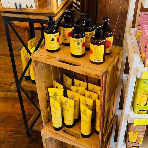 A display of "Naked Bee" brand lotions and soaps in yellow and pink packaging.