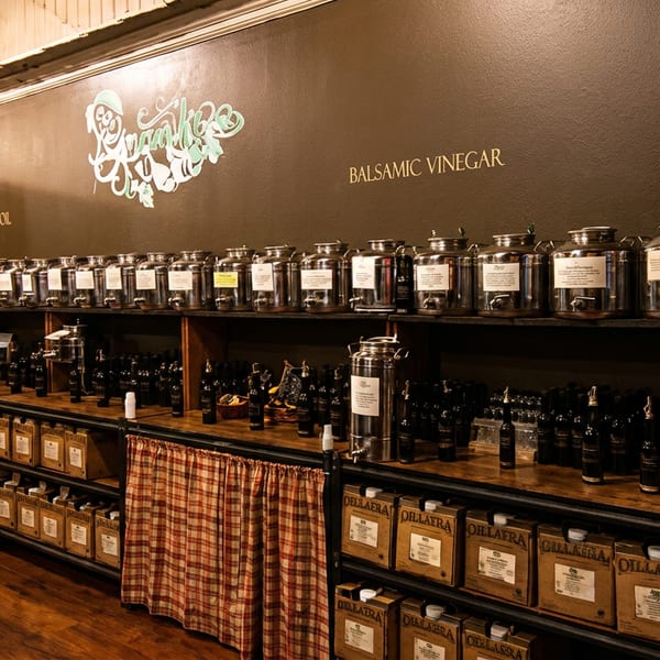 A store interior with shelves of olive oil and balsamic vinegar in large metal containers and bottles.