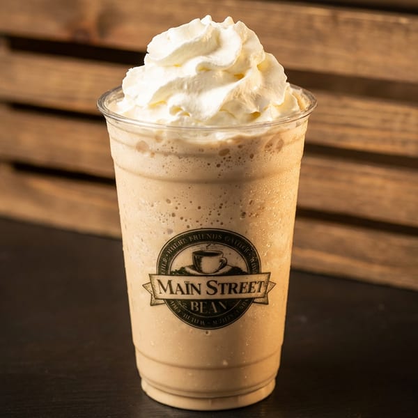 A Main Street Bean frappe with whipped cream sits on a dark surface in front of a wooden crate.